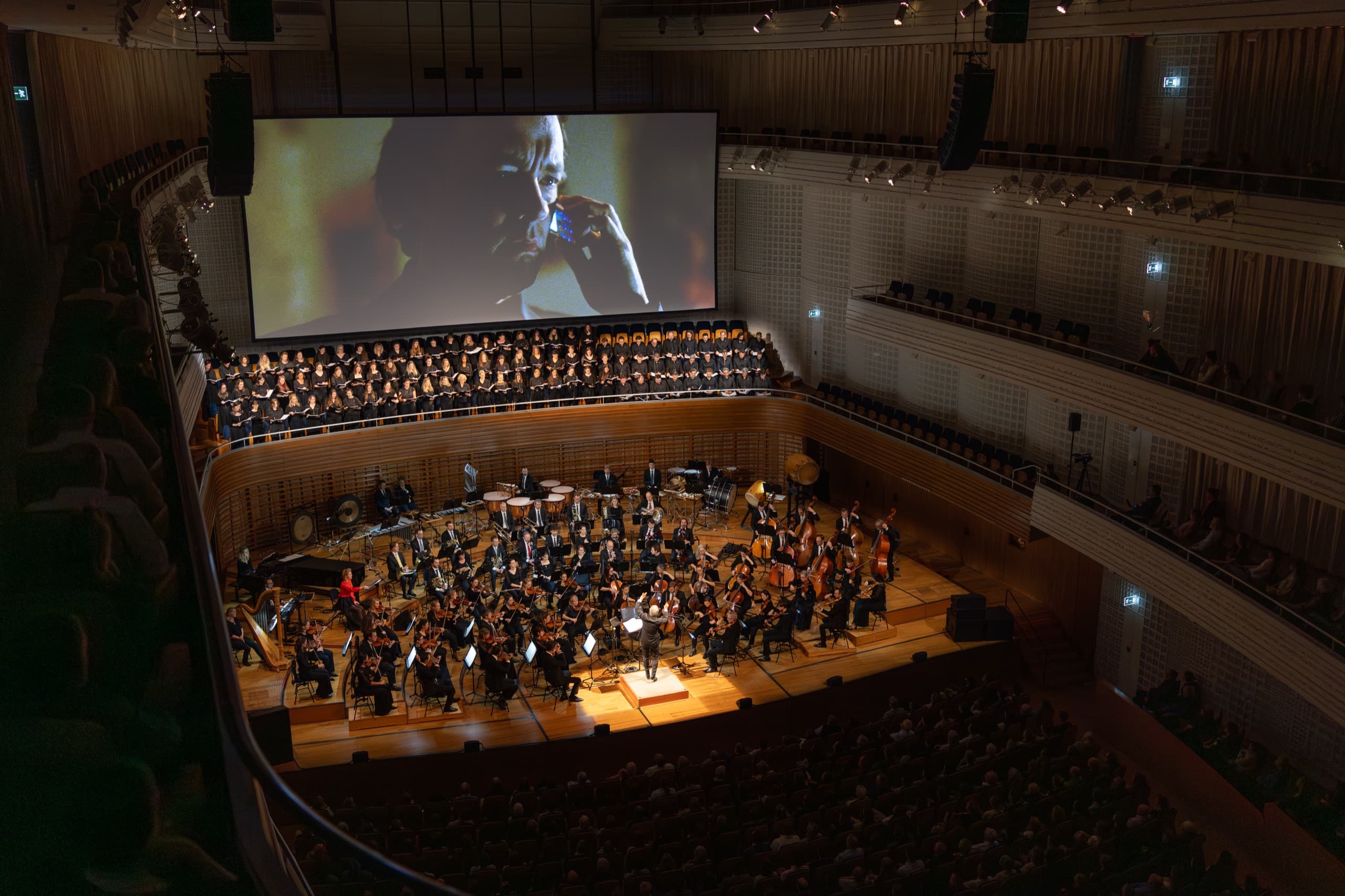 Blick von oben in den Konzertsaal des KKL Luzern: Orchester und Chor vor der Kinoleinwand